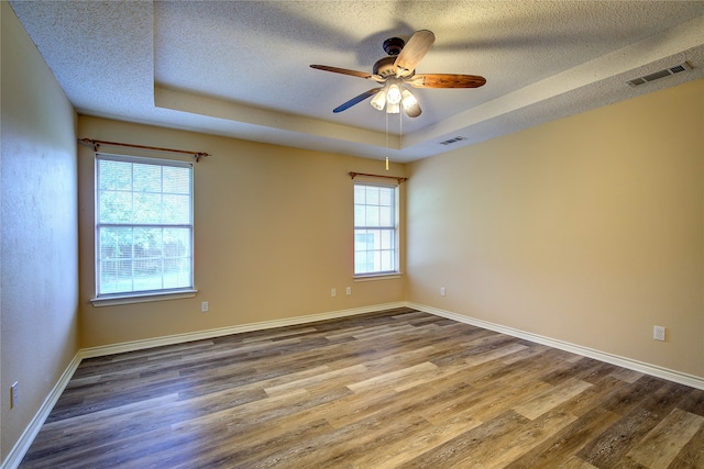 empty room featuring hardwood / wood-style floors, a healthy amount of sunlight, ceiling fan, and a tray ceiling