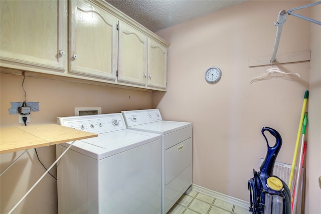 clothes washing area with light tile patterned flooring, washer and clothes dryer, a textured ceiling, and cabinets