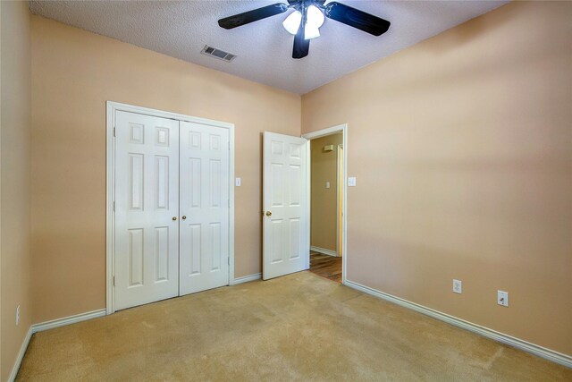 unfurnished bedroom with ceiling fan, light carpet, a closet, and a textured ceiling