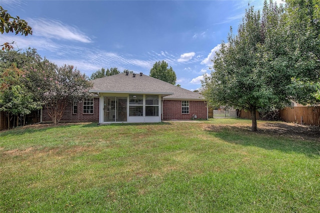 rear view of property featuring a sunroom, brick siding, a lawn, and a fenced backyard