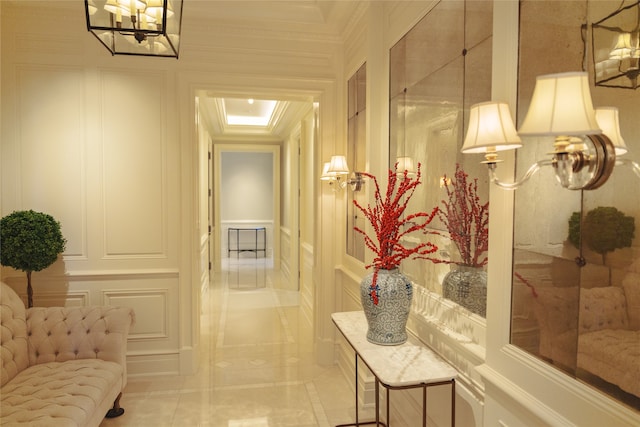 corridor with a raised ceiling, ornamental molding, a chandelier, and tile patterned floors