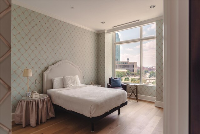 bedroom featuring a city view, crown molding, light wood-style flooring, baseboards, and wallpapered walls