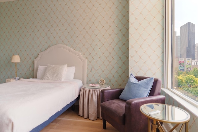 bedroom featuring wallpapered walls, light wood-style flooring, and a city view