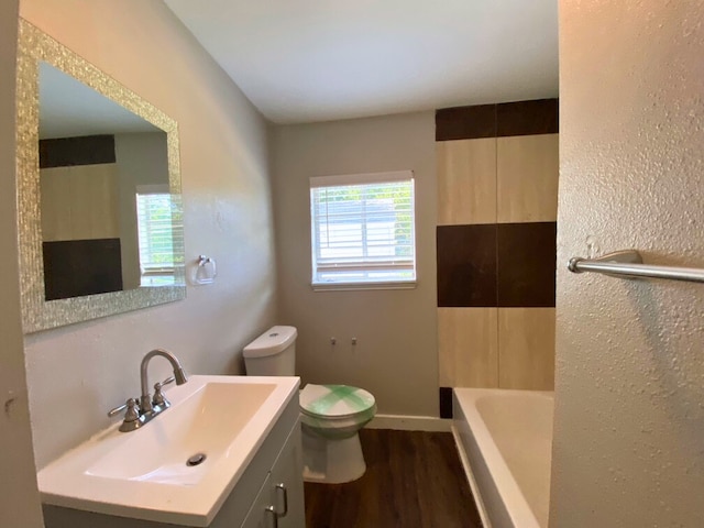 bathroom featuring wood-type flooring, a bath, vanity, and toilet