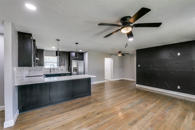 kitchen featuring light hardwood / wood-style floors, stainless steel refrigerator with ice dispenser, tasteful backsplash, ceiling fan, and kitchen peninsula