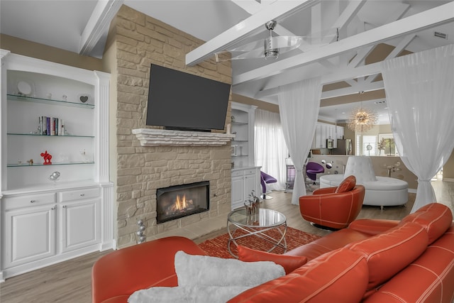 living room featuring hardwood / wood-style flooring, beam ceiling, a wealth of natural light, and a stone fireplace