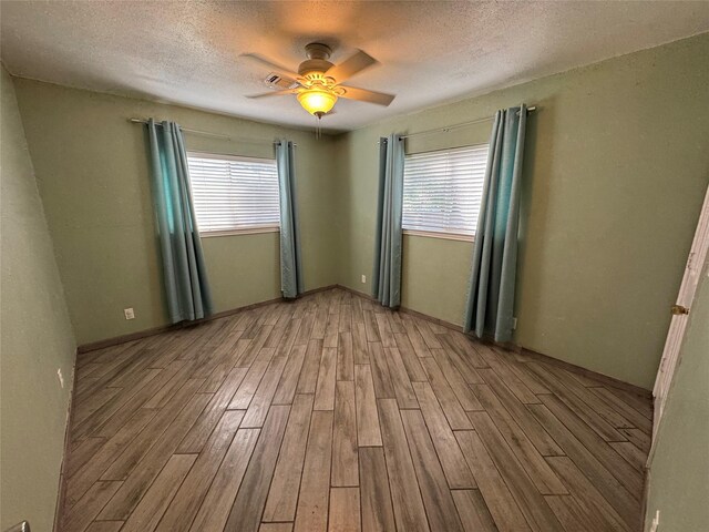 spare room with hardwood / wood-style floors, ceiling fan, a textured ceiling, and a healthy amount of sunlight