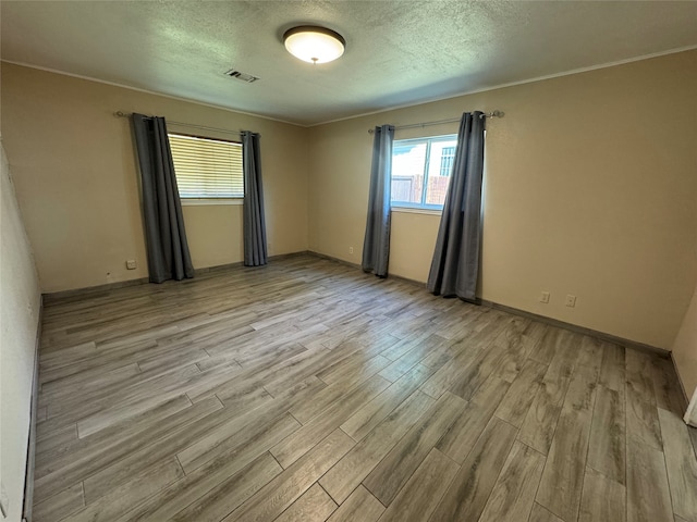 empty room with light wood-type flooring and a textured ceiling