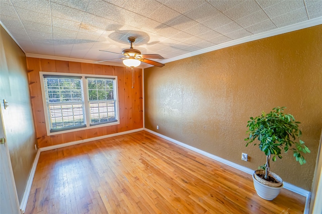 empty room with ceiling fan, wooden walls, light wood-type flooring, and ornamental molding