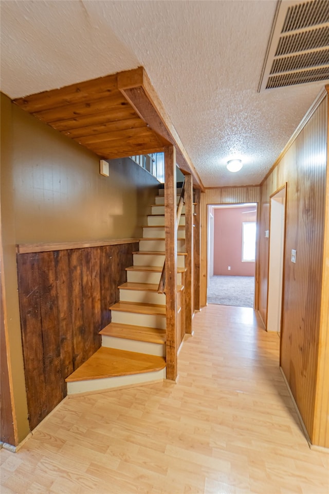 stairs with wood walls, carpet, and a textured ceiling