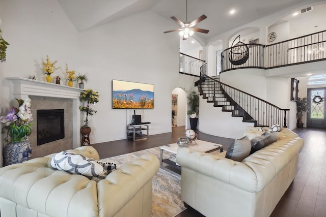 living room with ceiling fan, high vaulted ceiling, wood-type flooring, and a tiled fireplace