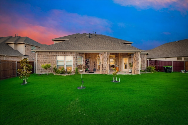 back house at dusk with a patio and a lawn