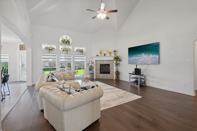 living room featuring ceiling fan, high vaulted ceiling, a tile fireplace, and dark hardwood / wood-style flooring