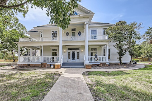 neoclassical home with a balcony, a front lawn, and covered porch