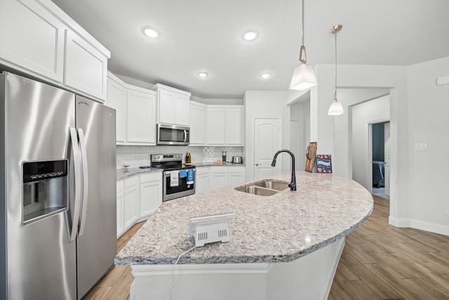 kitchen with hanging light fixtures, stainless steel appliances, sink, white cabinets, and tasteful backsplash