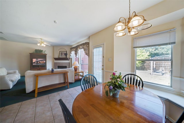 tiled dining area with a fireplace and ceiling fan with notable chandelier