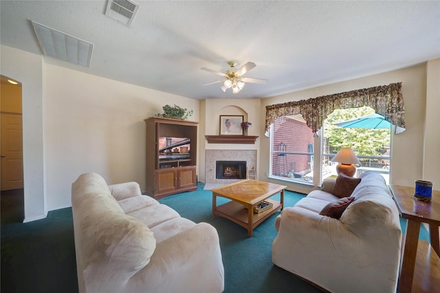 carpeted living room featuring ceiling fan, a textured ceiling, and a tiled fireplace