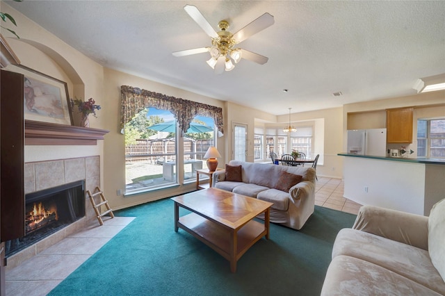 living room with a tile fireplace, light colored carpet, ceiling fan, and a textured ceiling