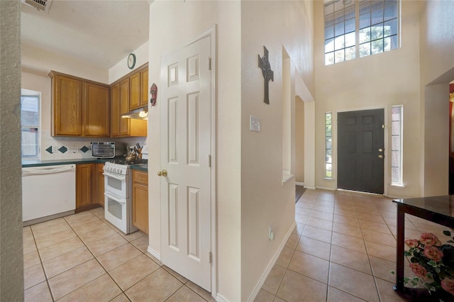 kitchen featuring white appliances, light tile patterned flooring, a high ceiling, and decorative backsplash