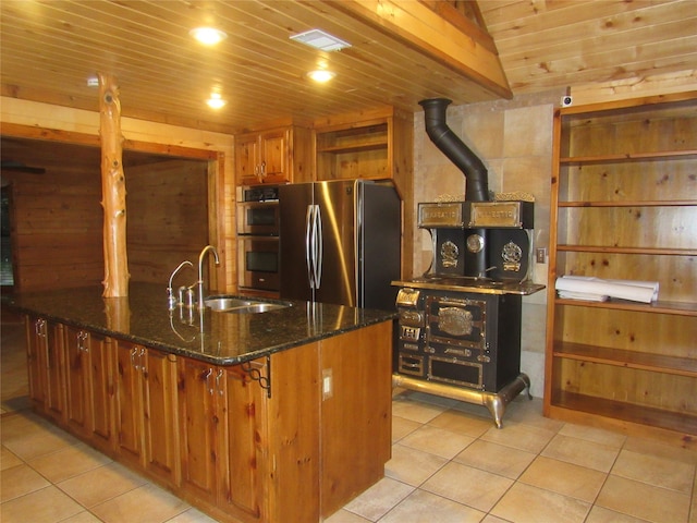 kitchen featuring vaulted ceiling, a wood stove, appliances with stainless steel finishes, sink, and light tile patterned flooring