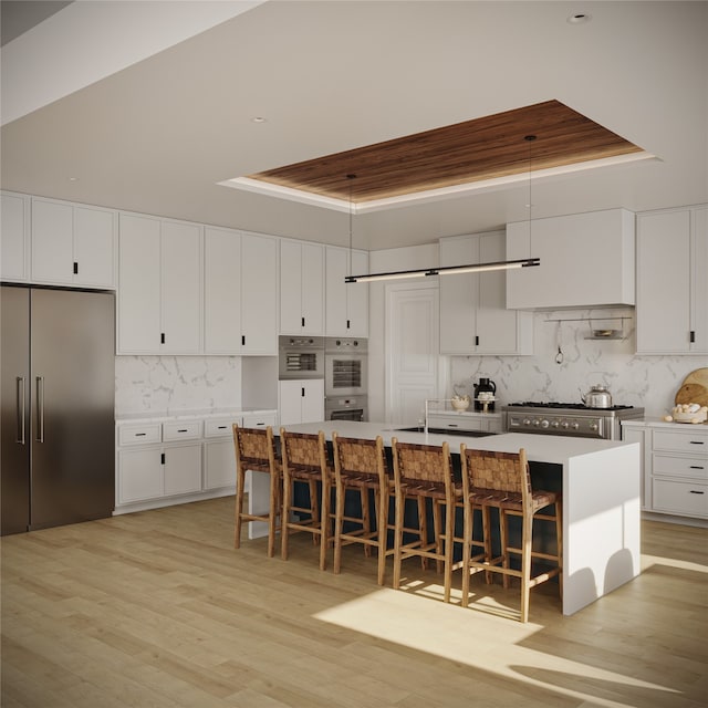 kitchen featuring a center island with sink, a breakfast bar area, stainless steel appliances, and a raised ceiling