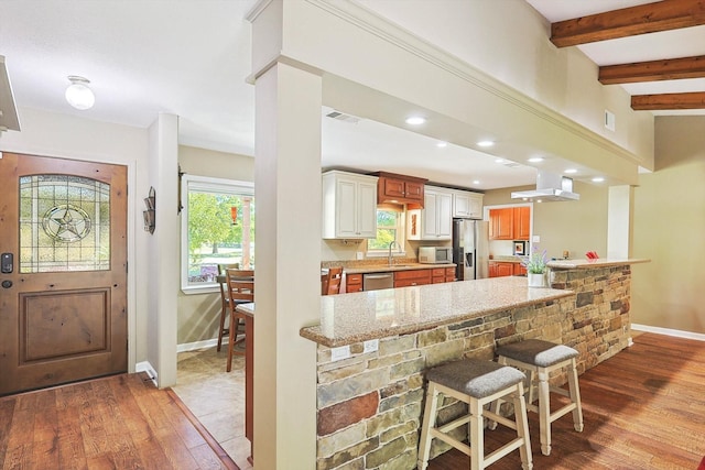 kitchen featuring wood-type flooring, stainless steel appliances, sink, light stone counters, and a breakfast bar area