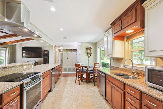 kitchen featuring appliances with stainless steel finishes, lofted ceiling with beams, wall chimney range hood, light stone counters, and sink