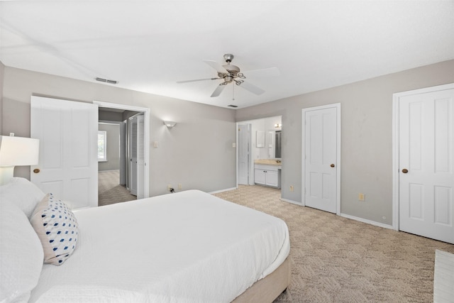 bedroom with two closets, light colored carpet, ceiling fan, and ensuite bathroom