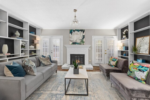 living room featuring built in shelves, french doors, wood-type flooring, a textured ceiling, and a fireplace