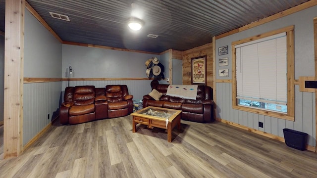 living room with wood walls, wood-type flooring, and ornamental molding