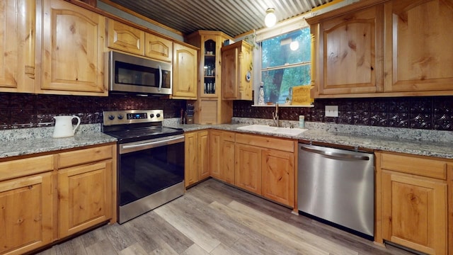 kitchen featuring decorative backsplash, appliances with stainless steel finishes, light stone countertops, light hardwood / wood-style floors, and sink