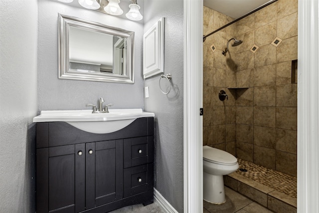 bathroom with tile patterned flooring, toilet, a tile shower, and vanity