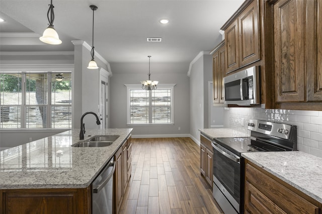 kitchen with appliances with stainless steel finishes, light stone counters, a center island with sink, and sink