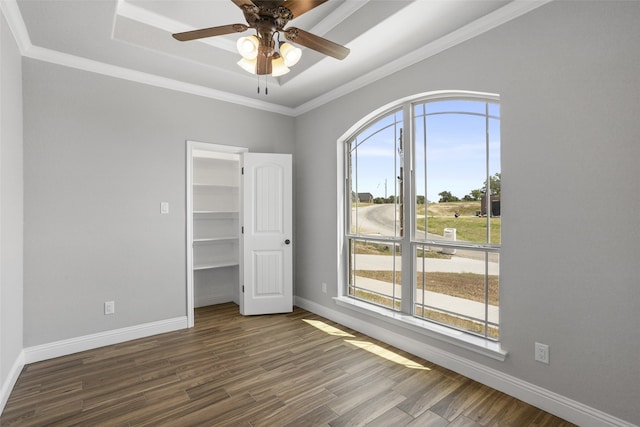 unfurnished bedroom featuring a closet, a tray ceiling, dark hardwood / wood-style floors, ceiling fan, and ornamental molding