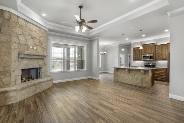 unfurnished living room with hardwood / wood-style floors, ceiling fan with notable chandelier, crown molding, a stone fireplace, and a tray ceiling