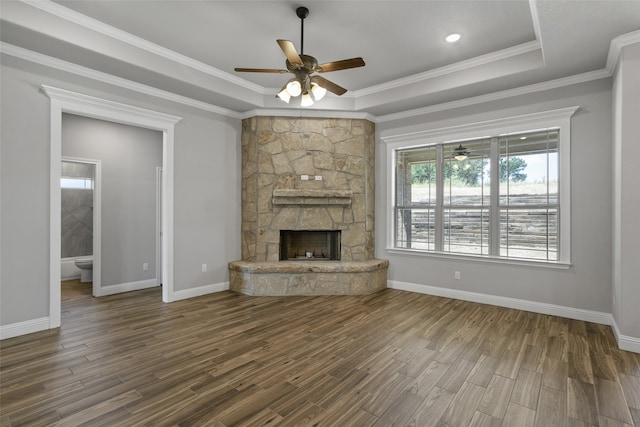 unfurnished living room with ceiling fan, a stone fireplace, wood-type flooring, and a tray ceiling