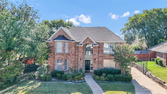 traditional home with a shingled roof, brick siding, and a front lawn