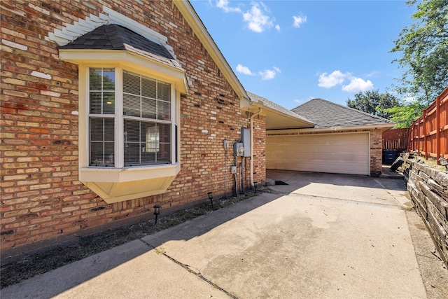 view of home's exterior with a garage, brick siding, driveway, and a shingled roof