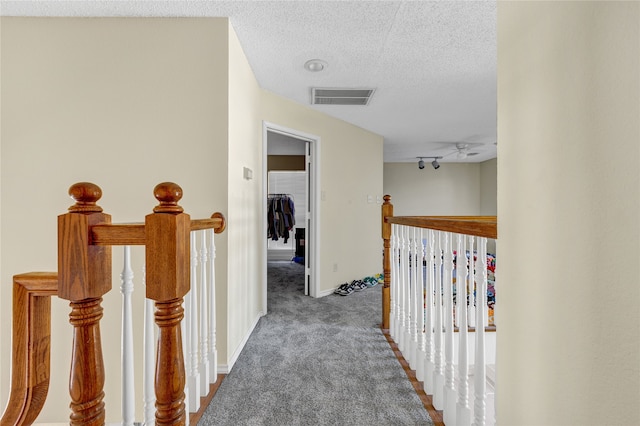 hallway featuring baseboards, visible vents, a textured ceiling, an upstairs landing, and carpet floors