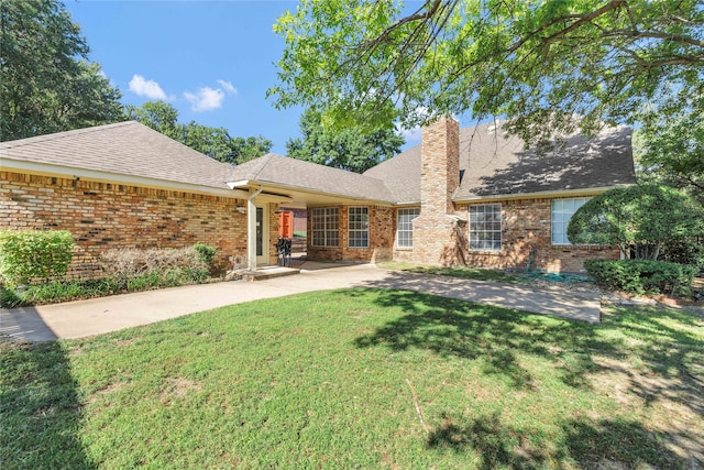 view of front of home featuring a shingled roof, brick siding, a chimney, and a front lawn