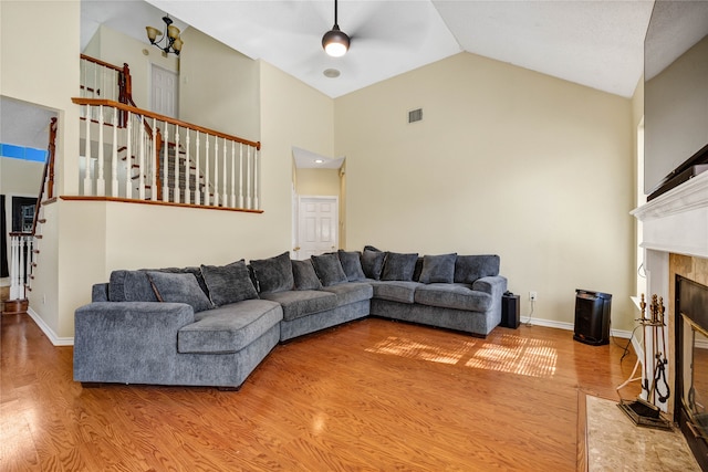 living area featuring high vaulted ceiling, wood finished floors, visible vents, stairs, and a tiled fireplace