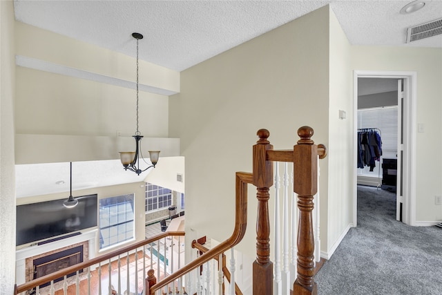 hallway featuring a textured ceiling, carpet flooring, an upstairs landing, visible vents, and an inviting chandelier