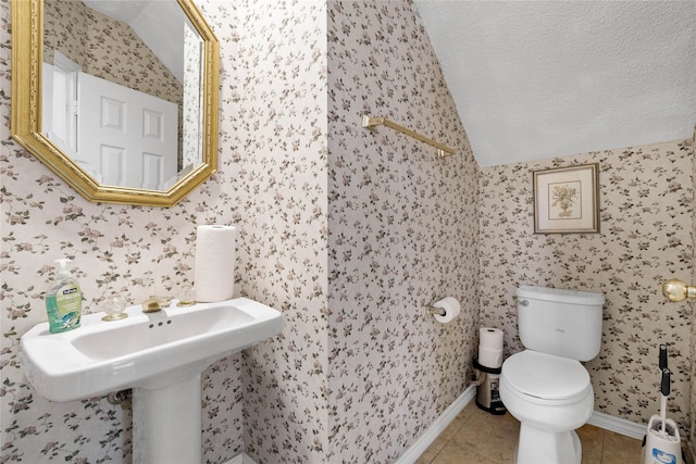 bathroom with lofted ceiling, toilet, tile patterned flooring, baseboards, and wallpapered walls