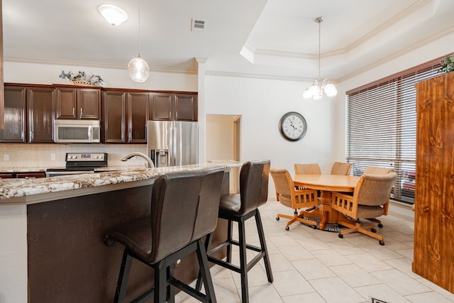 kitchen with ornamental molding, hanging light fixtures, light stone countertops, and stainless steel appliances