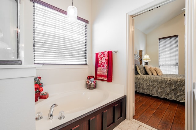 bathroom featuring a bathing tub, a healthy amount of sunlight, vaulted ceiling, and wood-type flooring