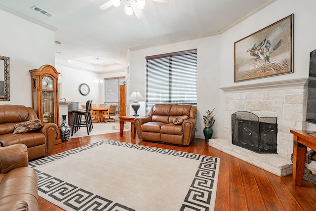 living room featuring hardwood / wood-style floors, crown molding, a stone fireplace, and ceiling fan