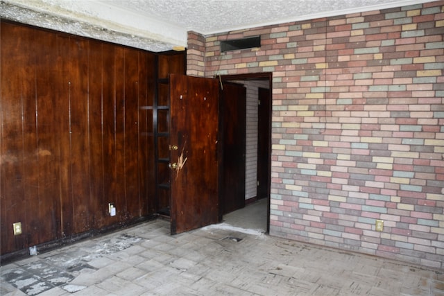 unfurnished room with wooden walls, a textured ceiling, and brick wall