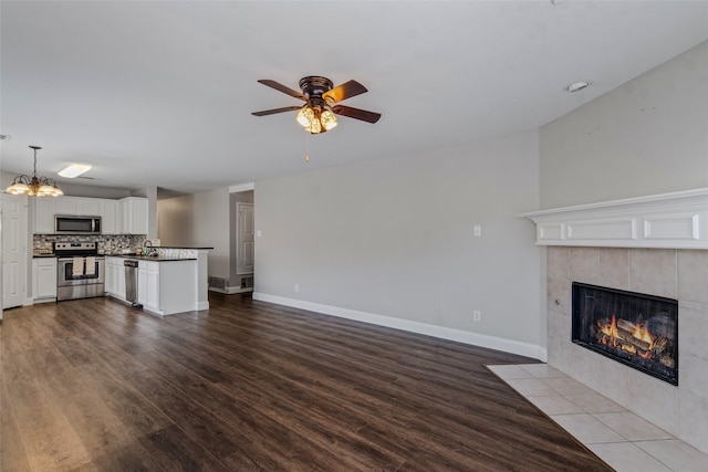 unfurnished living room featuring a fireplace, ceiling fan with notable chandelier, and light hardwood / wood-style floors