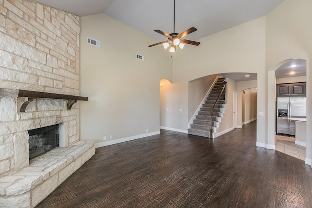 unfurnished living room featuring a stone fireplace, high vaulted ceiling, dark hardwood / wood-style floors, and ceiling fan