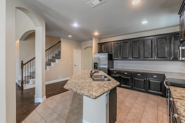 kitchen with sink, range with electric cooktop, stainless steel refrigerator with ice dispenser, light stone counters, and a center island with sink